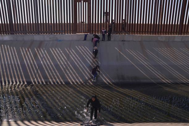 TOPSHOT - Migrants illegally cross into the United States from Mexico via a hole cut in the border fence in El Paso, Texas, US on December 21, 2022. - The southern border of the United States has been officially closed to immigrants without visas for more than two years under a controversial health measure invoked by then-president Donald Trump during the Covid-19 pandemic. Title 42 prevents asylum seekers from presenting themselves at ports of entry, allowing border patrol officers to turn them away without starting an asylum application. (Photo by Allison Dinner / AFP) (Photo by ALLISON DINNER/AFP via Getty Images)