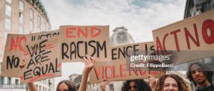People are marching on strike against racism in the city. They are holding cardboard signs.