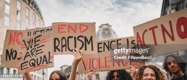 People are marching on strike against racism in the city. They are holding cardboard signs.